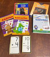 View of all learning workbooks and math flashcards in the bundle arranged on a table, colorful covers with cartoon animals such as monkey and alligator, and flashcards with mathematical addition and subtraction problems.