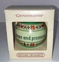 Front view of original box with window showing the spherical ornament with knit pattern and partial text 'hope and promise'. Box labeled 'Granddaughter' and 'Keepsake Ornament'.