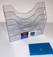 Front angle view of clear 3-tier Rubbermaid organizer with small blue folder in front