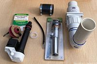 Photo showing the entire lot with Zoeller check valve attached to PVC pipe, toilet fill valve with flapper, chrome sink drain pipe, hose clamp, black hose, and white Teflon tape.