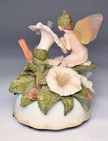 Front and top view of the music box showing the fairy figurine kneeling among white bindweed flowers with fiber optic stamens and detailed green leaves on the base.