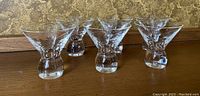 Six short clear glasses shown in a row, displaying their wide bowl and thick base with etched floral pattern.