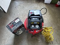 Red Central Pneumatic 3 gallon oilless air compressor with yellow coiled hose and Craftsman spray gun box next to it.