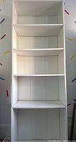 Front view of tall white bookshelf showing five shelves with adjustable holes along sides.