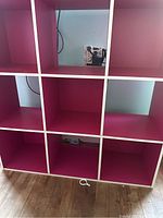 Front view of pink cube storage unit showing 9 square compartments in a 3x3 grid, placed on wooden floor with visible power outlet behind.
