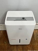 Front view of Midea dehumidifier showing control panel on top and brand logo.