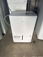 Full front view of the white Midea dehumidifier showing brand logo and water level indicator at the bottom.