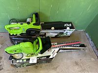 Electric gardening tools including two green electric chainsaws and two green electric hedge trimmers along with branded boxes in background