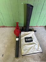 Photo showing Toro electric leaf blower and vacuum with detachable black nozzle and white collection bag against green wall on floor.