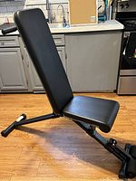 Exercise bench set up in upright position showing padded backrest and seat with metal frame on wood floor.