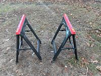 Pair of black plastic sawhorses with red tops standing on grass outdoors.