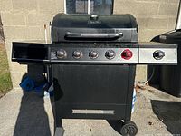 Full front view of the black Dyna-Glo gas grill with six control knobs and side burner, showing the grill and side shelves.