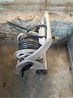 Side view of coiled black garden hose on a beige plastic reel with handle and wheels.
