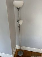 Full view of metal floor lamp with round base and two white frosted glass shades in a corner of a room.