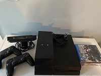 PlayStation 4 console with two internal hard drives attached, two black DualShock 4 controllers, PlayStation Camera, power cable, and four PS4 game cases displayed on a table.