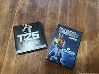 Two DVD workout training programs on a wooden surface: Beachbody Focus T25 Get It Done and Billy Blanks Taebo Ripped.