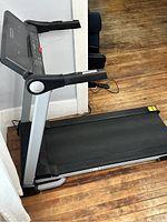 Side view of the treadmill showing running belt, foldable frame, and handrails on wood floor