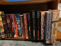 Books shelf showing fantasy novels by Karl Edward Wagner, Joe Abercrombie, Robert E. Howard, and others, tightly packed on a wooden shelf.