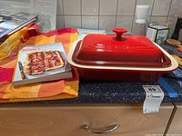 Red Le Creuset casserole dish with lid and Simply 5 cookbook on kitchen countertop.