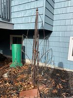 Full view of weathered metal garden alarise in ground surrounded by soil and leaves in front of blue siding house.
