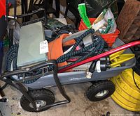 Full view of garden cart loaded with various gardening supplies including hoses, kneeling pads, buckets, and packages of grass seed.