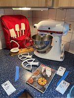 Front-left view showing mixer, bowl, attachments on countertop, red cloth cover with spatulas, and recipe book.