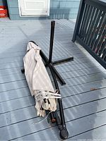 Folded beige fabric umbrella with attached black metal frame and crank handle lying on deck floor alongside black metal four-legged umbrella base stand.