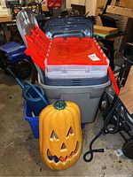 Overview of the stacked plastic storage bins, including large grey bin and three smaller clear bins with red lids, brand not visible here. Also a pumpkin decoration and other items around.