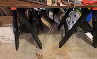 Two black plastic saw horses positioned side by side with visible shelf tops under a workbench.