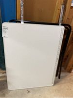 Full view of white folding table leaning against wall showing the tabletop and folded legs behind it.