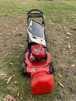 Front view of Toro lawn mower with attached grass collection bag and gas can in front.