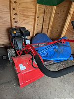 Front left side view of red Troy-Bilt Super Bronco rototiller showing engine, handle, and tines.