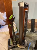Full view of Bissell Air Ram vacuum cleaner next to Lasco tower fan showing their size and colors.
