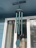 Front view of metal wind chime showing four green tubes and circular striker