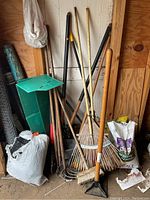 Full view of garden tools including rakes, hoes, broom, and bags on floor.