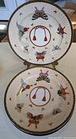 Two china plates showing crackle glaze surface with multicolored butterfly designs and central red circular tassel motif.