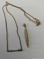 Photo showing a gold-tone chain necklace with lobster clasp and extender chain, alongside an elongated rhinestone pendant.