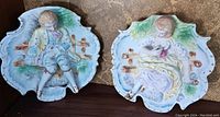 Front view of the two bisque porcelain wall plaques depicting male and female figures in period costume, showing colors, details and size.