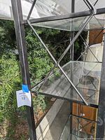 Close-up image showing the black metal frame and one of the glass shelves with cross-braced support behind it.