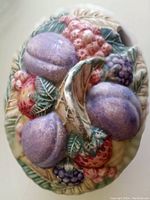 Close-up of colorful fruit decoration on porcelain jar lid showing plums, raspberries, and leaves