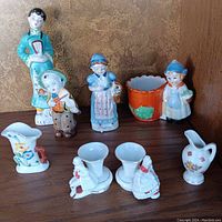 Front view of eight porcelain figurines and small vases including Asian and European characters and floral designed pieces.