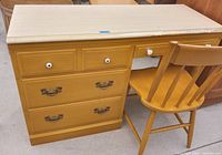 Front angle view showing desk with honey oak finish, three drawers on the left side with two metal handles and one white knob, and one smaller drawer on right with two white knobs, plus matching wooden chair.