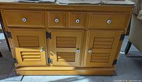 Front view of the wooden mid century sideboard showing four drawers on top and three cabinet doors below with white round knobs and louvered door panels.