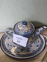 Photo of the ceramic teapot with lid, floral pattern in blue, yellow, and orange on cream background
