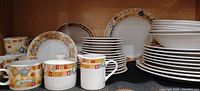 Front view of the Majesticware by Sakura dish set showing various plates, bowls, cups, and sugar/creamer set all featuring the multicolor diamond pattern.