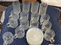 Full set of glassware including tall glasses, cups with handles, saucers, and additional pieces, all placed on a blue padded moving blanket.