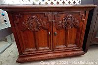Front view of vintage end table showing two carved wooden doors with ornate decoration and door knobs.