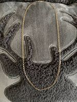 Full length of the gold and sterling silver Cuban style chain laid flat on a textured surface.