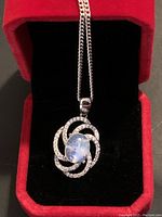 Front view of the pendant and chain in red jewelry box showing the moonstone oval cabochon surrounded by topaz stones in sterling silver swirl design.
