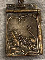 Front view of brass pendant showing embossed swan and floral design, pendant closed